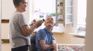 Person with a bowl and spoon in their hand to feed a person with Cerebral Palsy