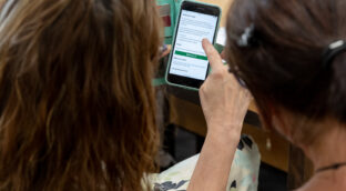 The back of two people looking at the PA noticeboard on a mobile phone