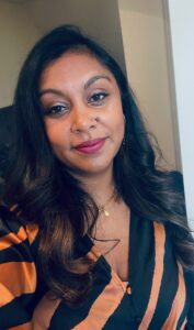 Picture of DPSO Darshna Pancholi smiling wearing an orange and black striped top