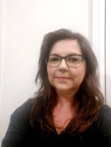 Picture of a smiling woman, wearing glasses and long hair.